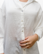 Woman in white satin button-down shirt and jeans.