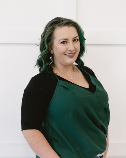 A woman with green hair wearing a black top with elbow sleeves and a V-neck.