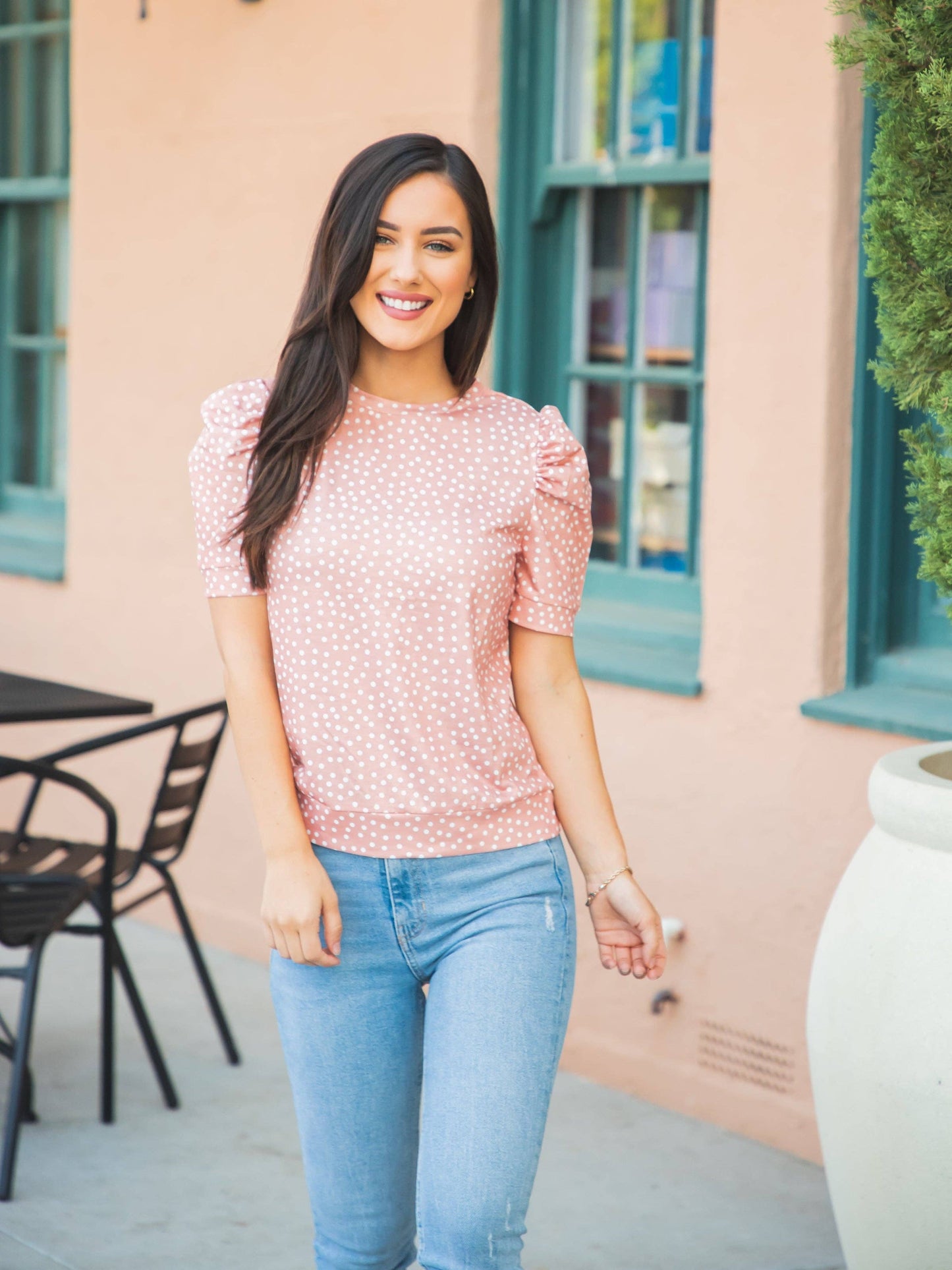 A woman confidently displays her lively style in a red floral top and jeans, set against a neutral backdrop.