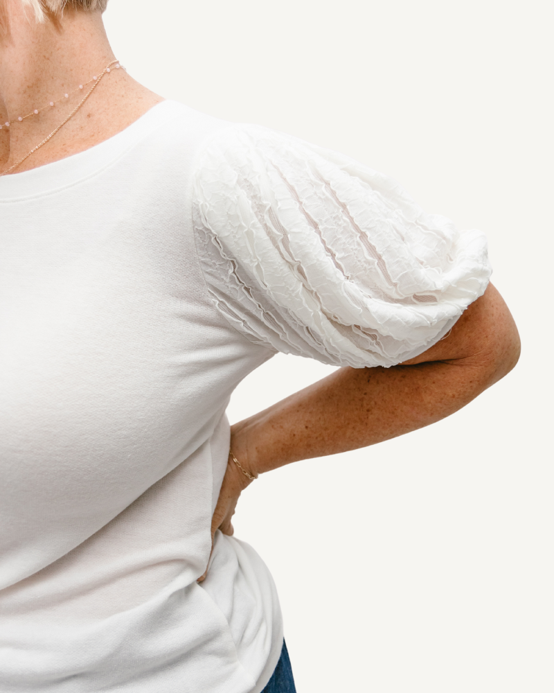 A woman in a white shirt experiencing back pain. She is wearing a Solid Full Tee with Contrast Sleeve.