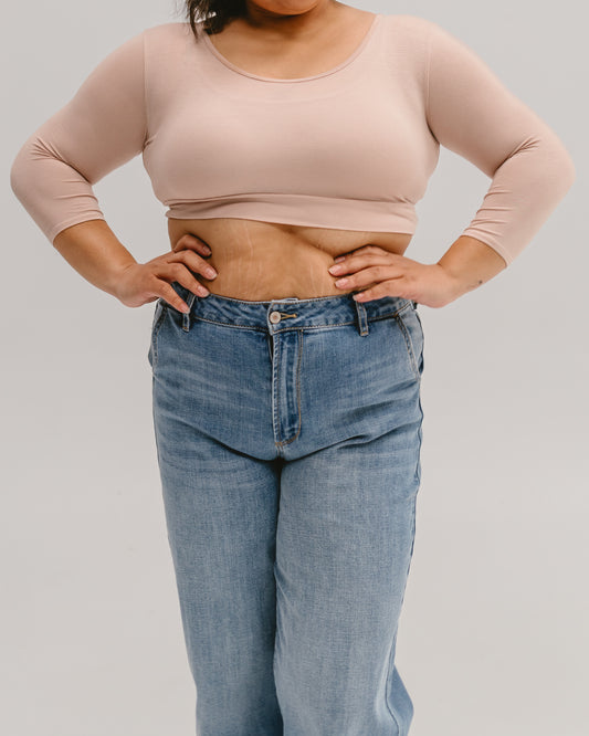 A cropped view of a person wearing a beige Halftee with three-quarter sleeves and high-waisted light-wash jeans, standing with hands on hips.