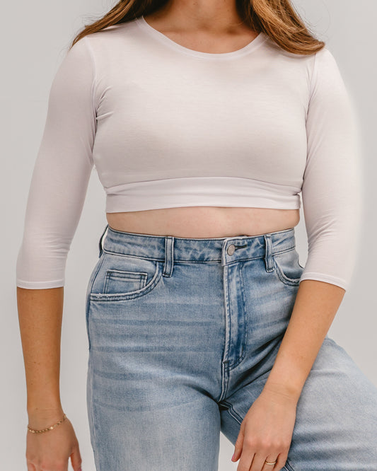 A cropped view of a person wearing a fitted white Halftee with three-quarter sleeves and high-waisted light-wash jeans.