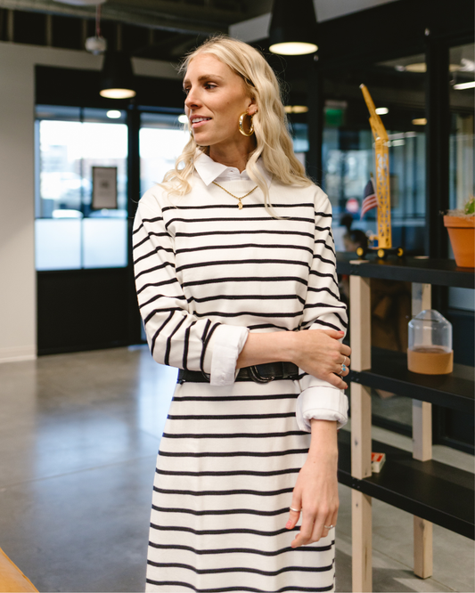A woman in a striped dress stands confidently in a modern office setting, showcasing a professional atmosphere.