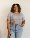 A woman with curly hair and a bright smile showcases a crop top from HALFTEE Layering Fashions, embodying modern fashion.