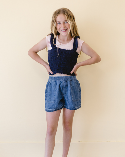 A young girl in a pink shirt and jeans, standing next to a sign that reads 'GIRLEE Boyfriend'.