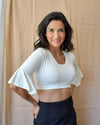 A woman wearing a white crop top and jeans, showcasing a Bell Sleeve Halftee.