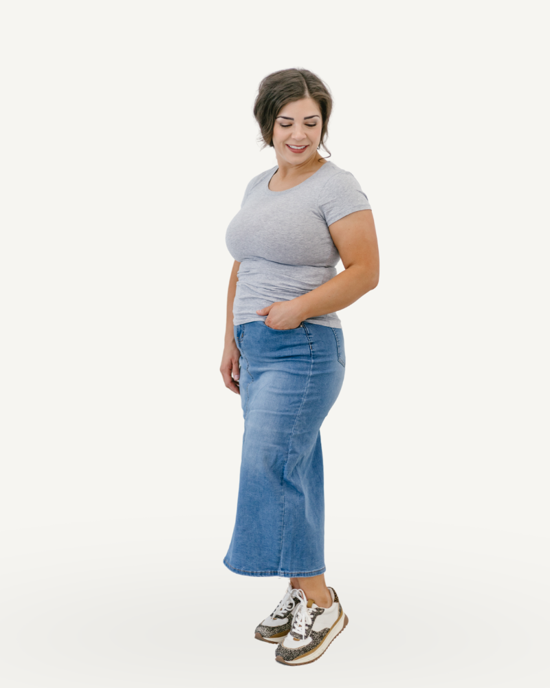 A girl wearing a denim skirt and a gray shirt stands confidently, showcasing a casual yet stylish outfit.