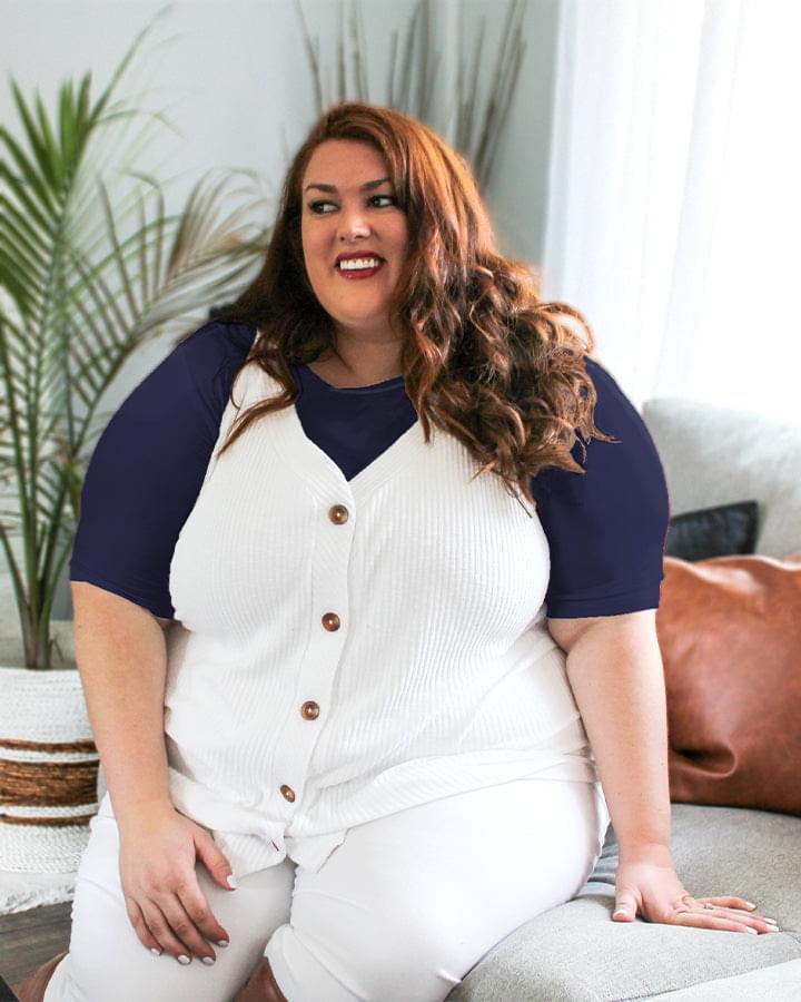 A woman wearing a navy crew neck elbow sleeve top and white shirt.