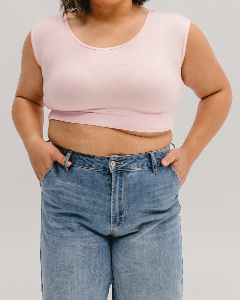 Pink crop top and blue jeans on a woman with dark hair, standing against a light background with her hands in her pockets.