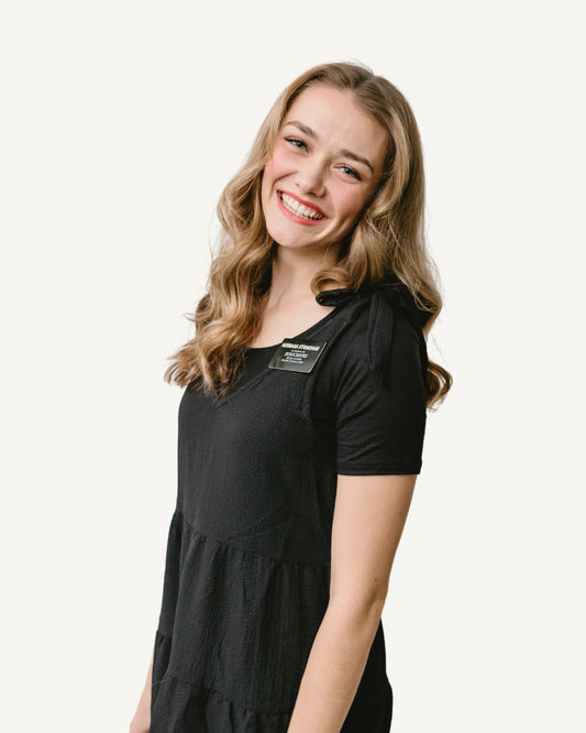 A smiling young woman in a black dress, holding an Essential Missionary Pack black.