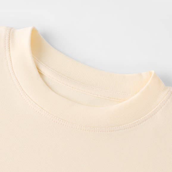 Close-up of a soft cream t-shirt's neckline, showcasing fine stitching and smooth fabric texture. The tone is minimalist and comforting.