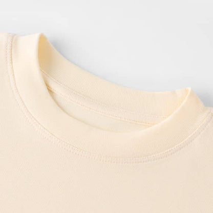 Close-up of a soft cream t-shirt's neckline, showcasing fine stitching and smooth fabric texture. The tone is minimalist and comforting.