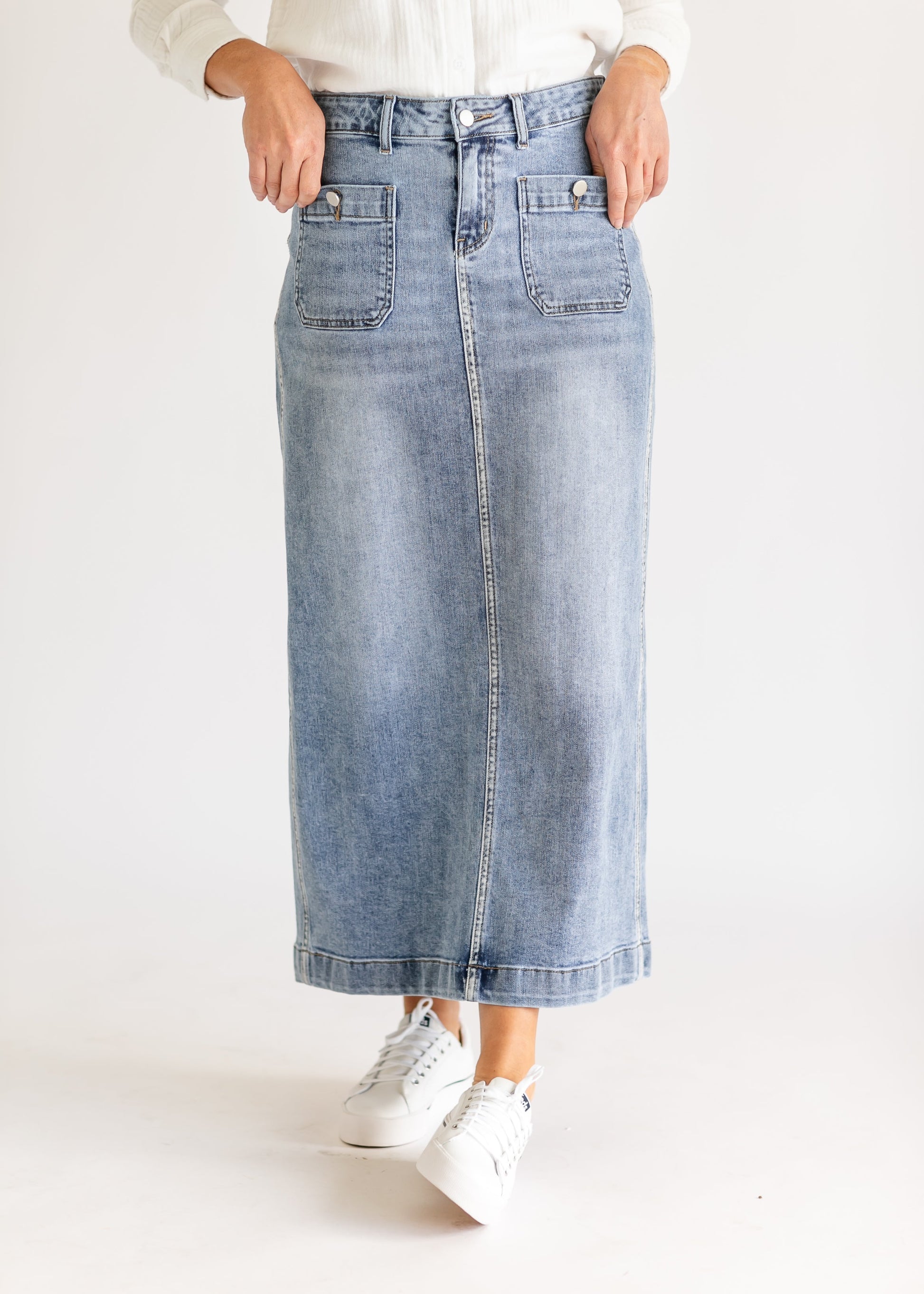Close-up of a person wearing a white textured top and light gray denim skirt. One hand is casually placed in the skirt's pocket, creating a relaxed vibe.
