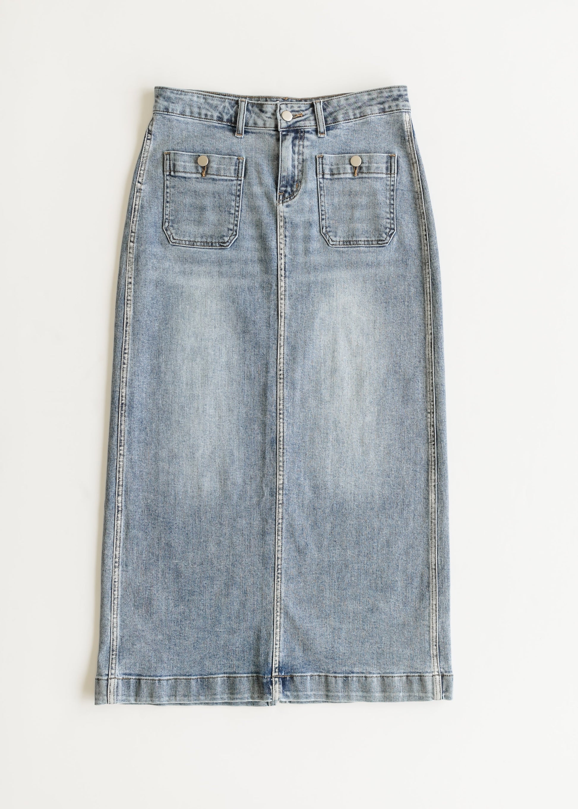 Light blue denim skirt with a straight fit, features two front pockets, button closure, and seam detailing. The tone is casual and stylish.