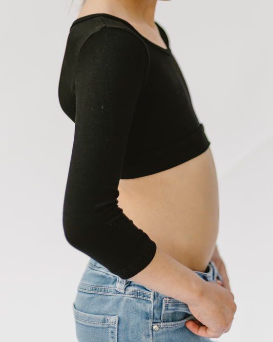 Person in a black crop top and blue jeans, shot from the side. The focus is on the outfit, highlighting the fit and style. The mood is casual and relaxed.