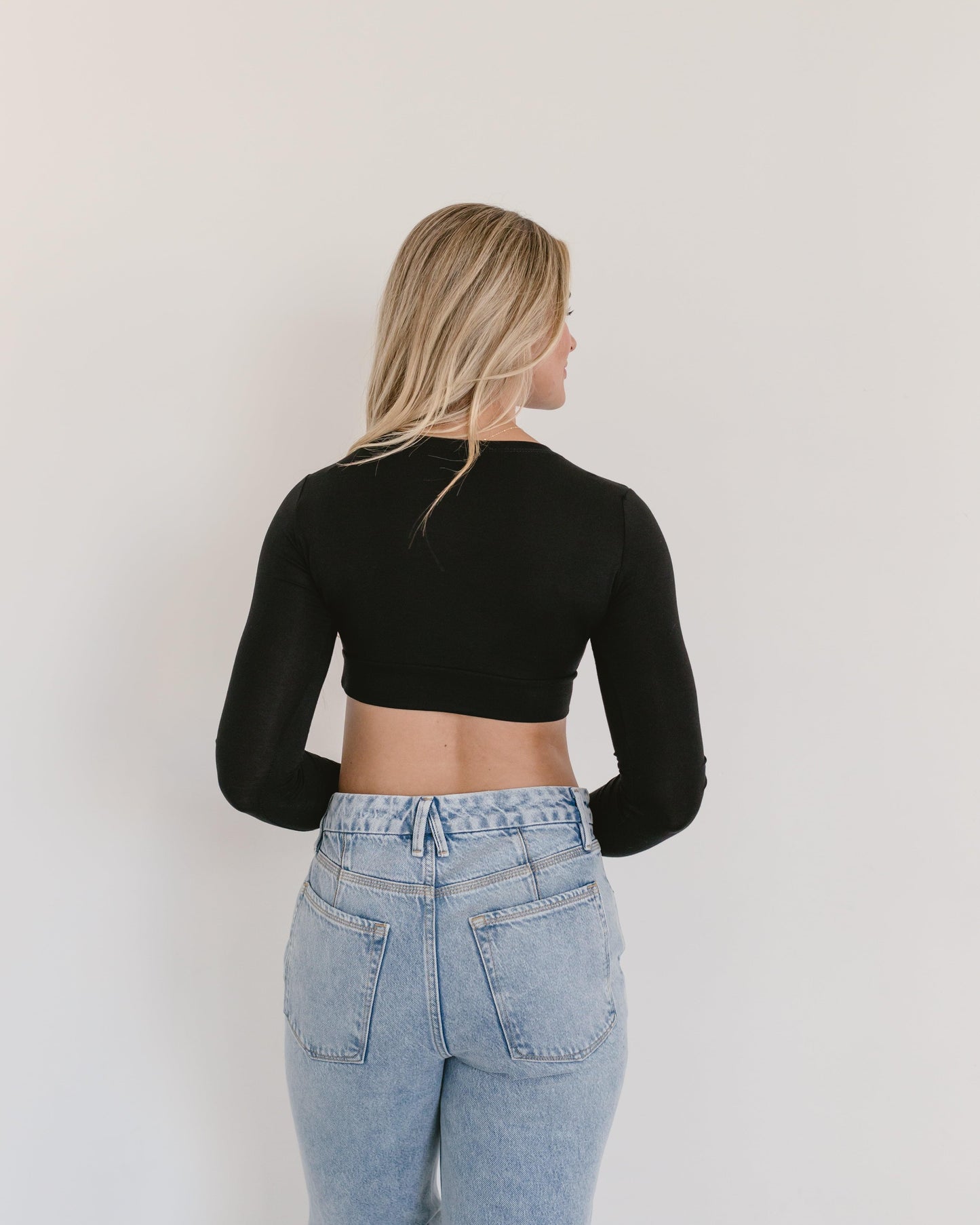 A woman wearing a black crop top and jeans, with a crew neck long sleeve.