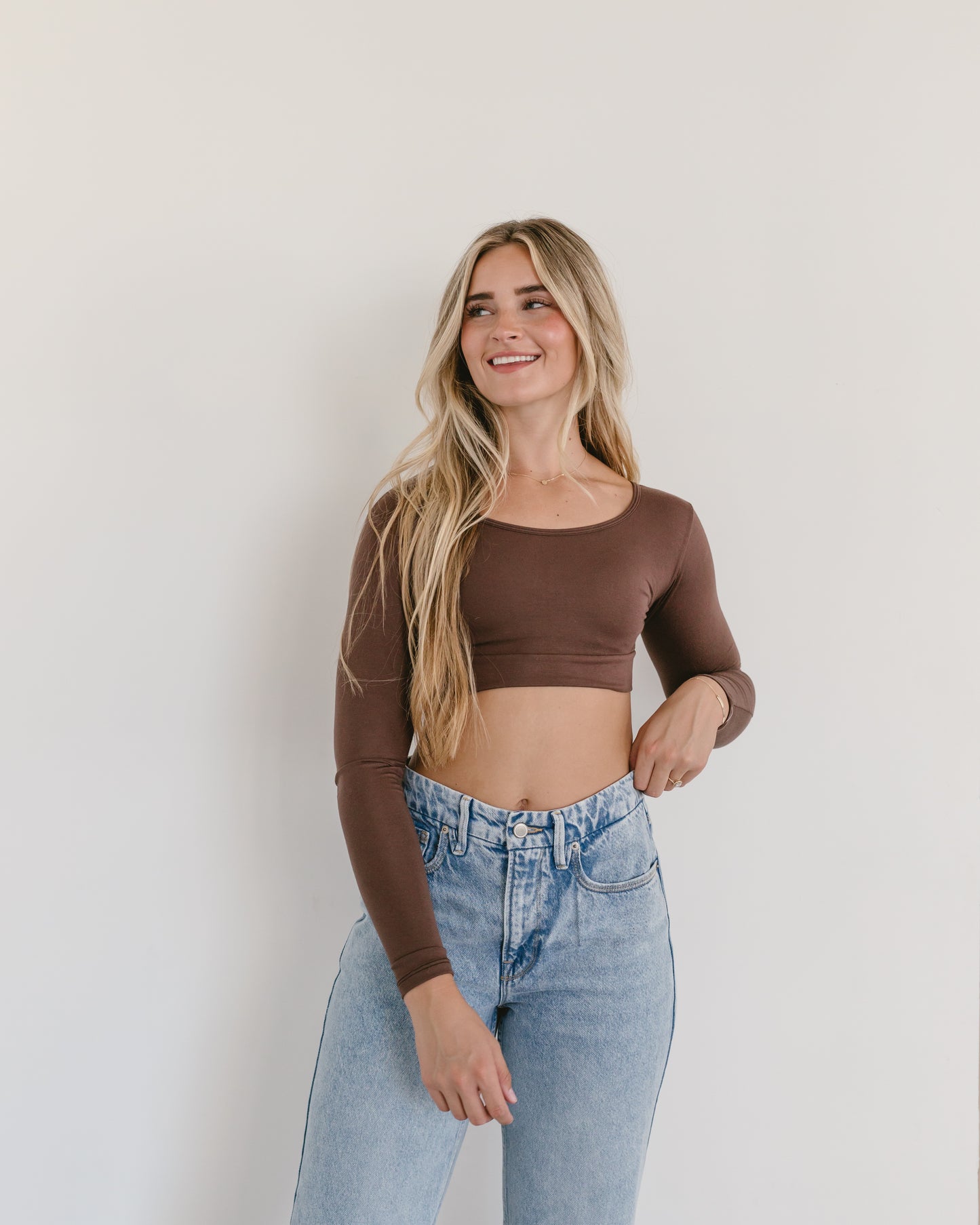 A woman in a brown crop top and jeans, wearing a Classic Long Sleeve Halftee.