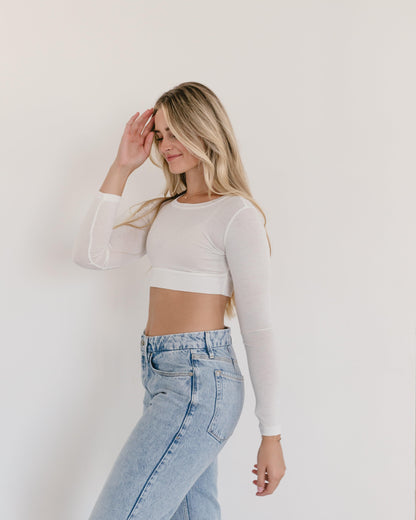 A woman wearing a white crop top and jeans, with a crew neck long sleeve.