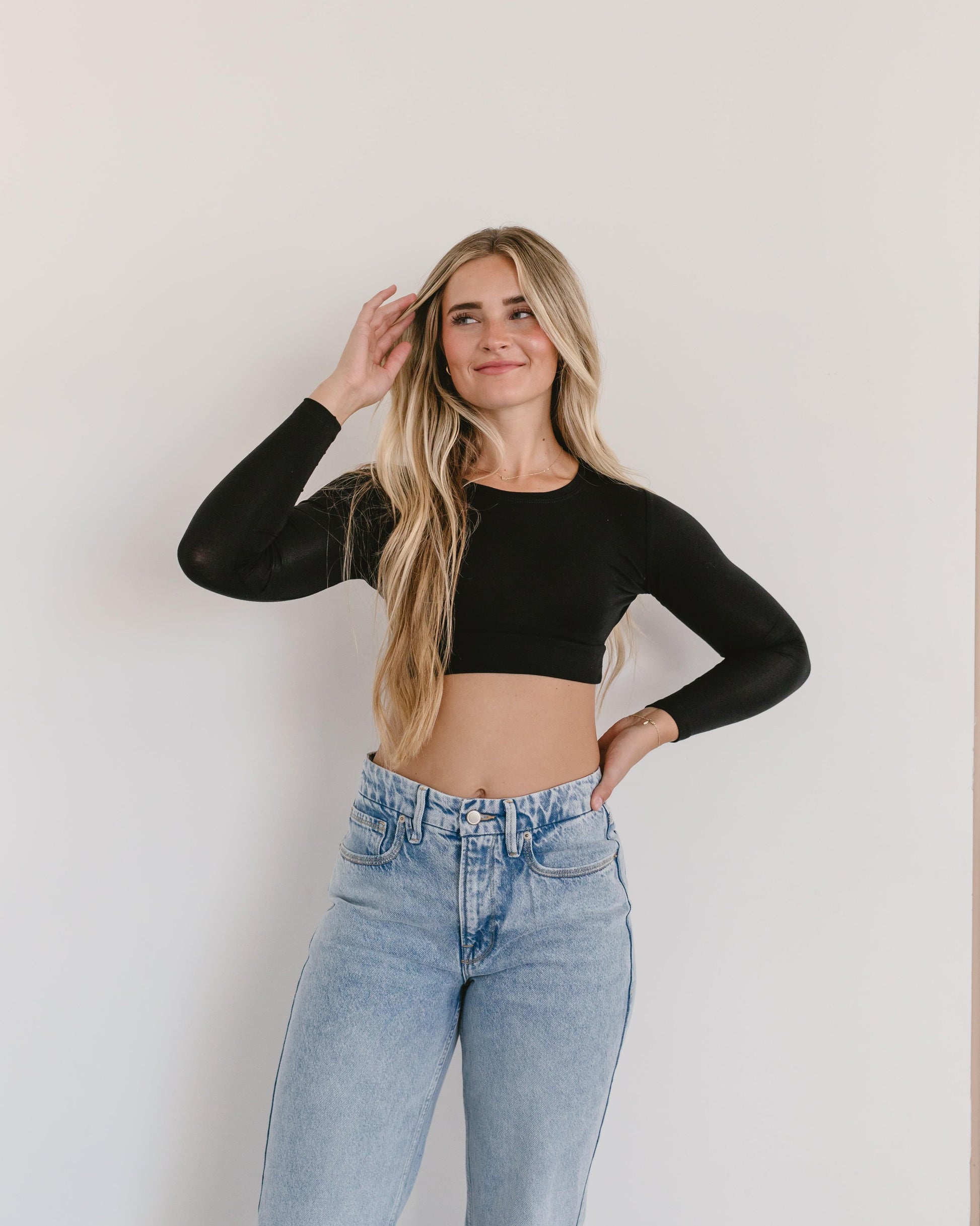 A woman wearing a black crop top and jeans, with a crew neck long sleeve.