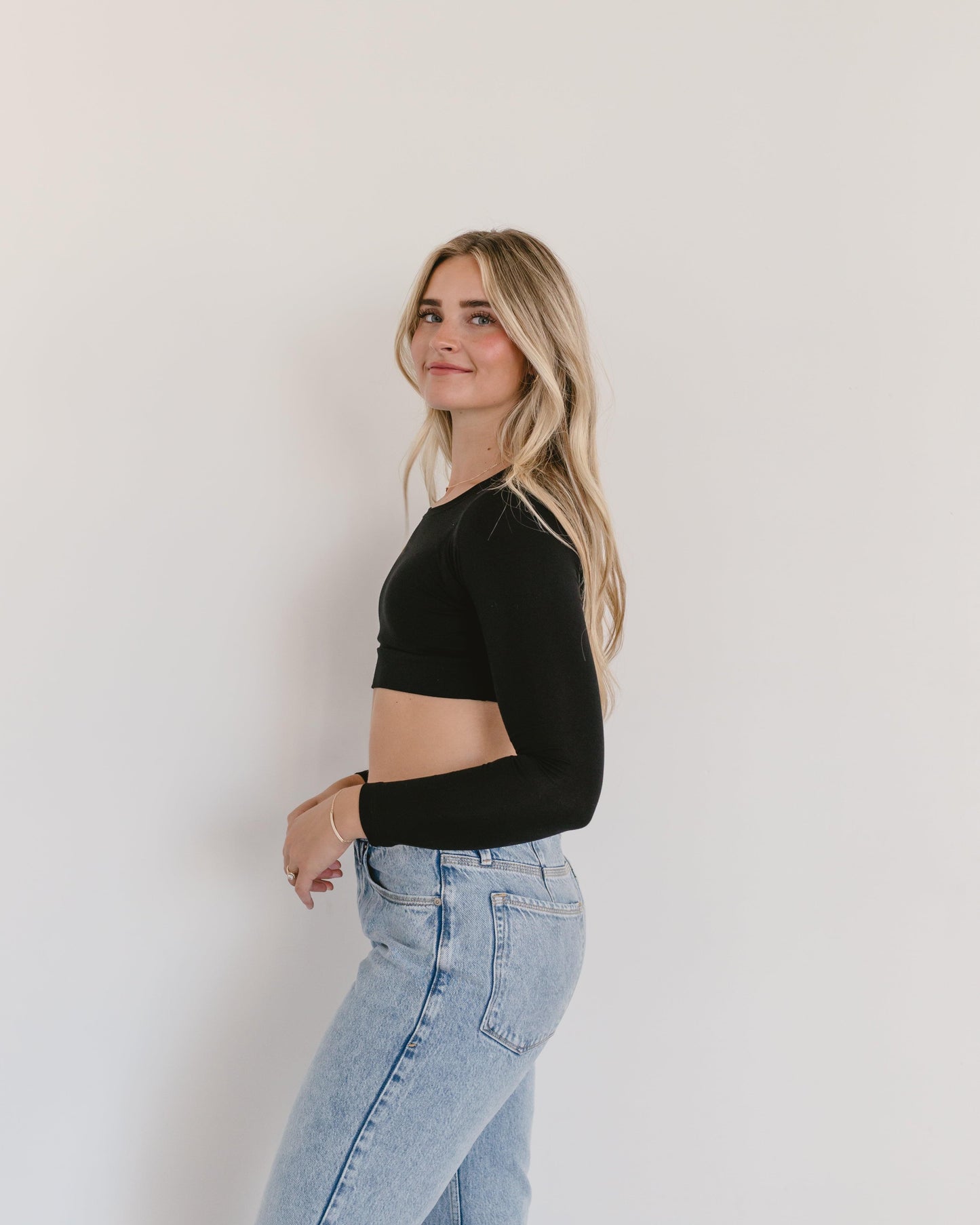 A woman wearing a black crop top and jeans, with a crew neck long sleeve.