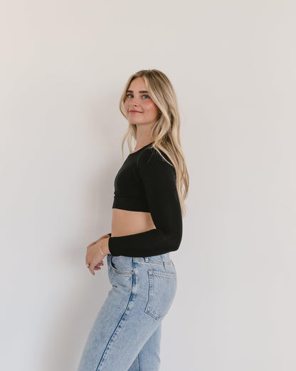 A woman wearing a black crop top and jeans, with a crew neck long sleeve.