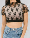 Close-up of a person's torso and arms wearing a black lace crop top, a light underlayer, and denim jeans.