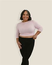 A woman wearing a pink top and black pants stands confidently, showcasing a stylish and modern outfit.