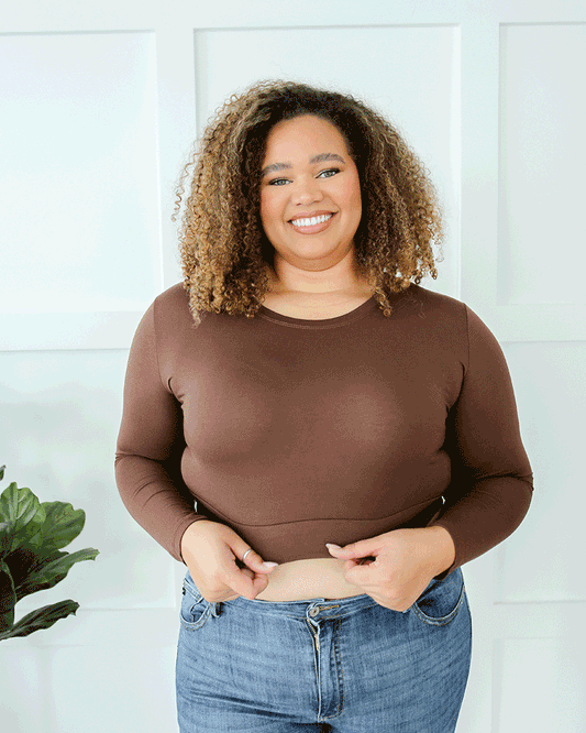 A woman wearing a brown crop top and jeans, with a crew neck long sleeve.