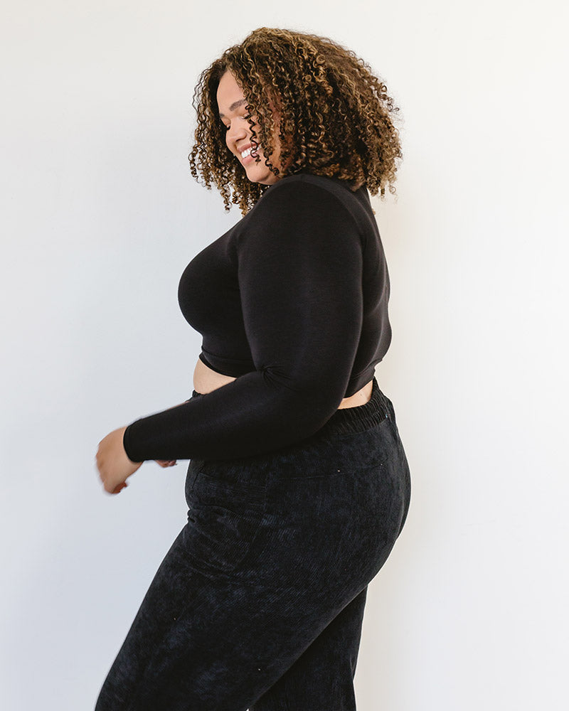 A woman wearing a black turtle neck sweater and black pants. She is also wearing a 'Mock Long Sleeve' garment.