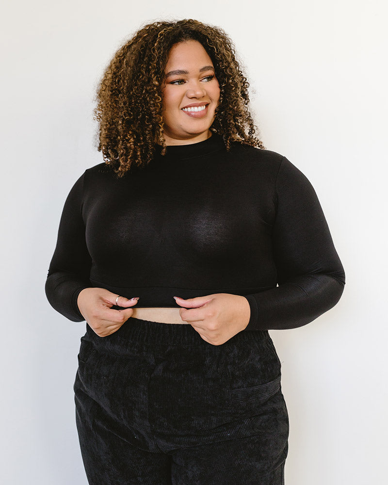 A woman wearing a black turtle neck sweater and black pants. She is also wearing a 'Mock Long Sleeve' garment.
