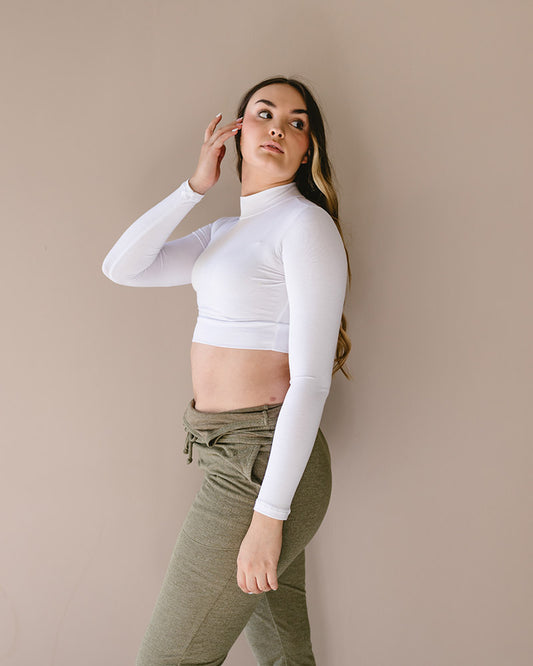 A woman wearing a white turtle neck sweater and green pants. She is also wearing a 'Mock Long Sleeve' garment.