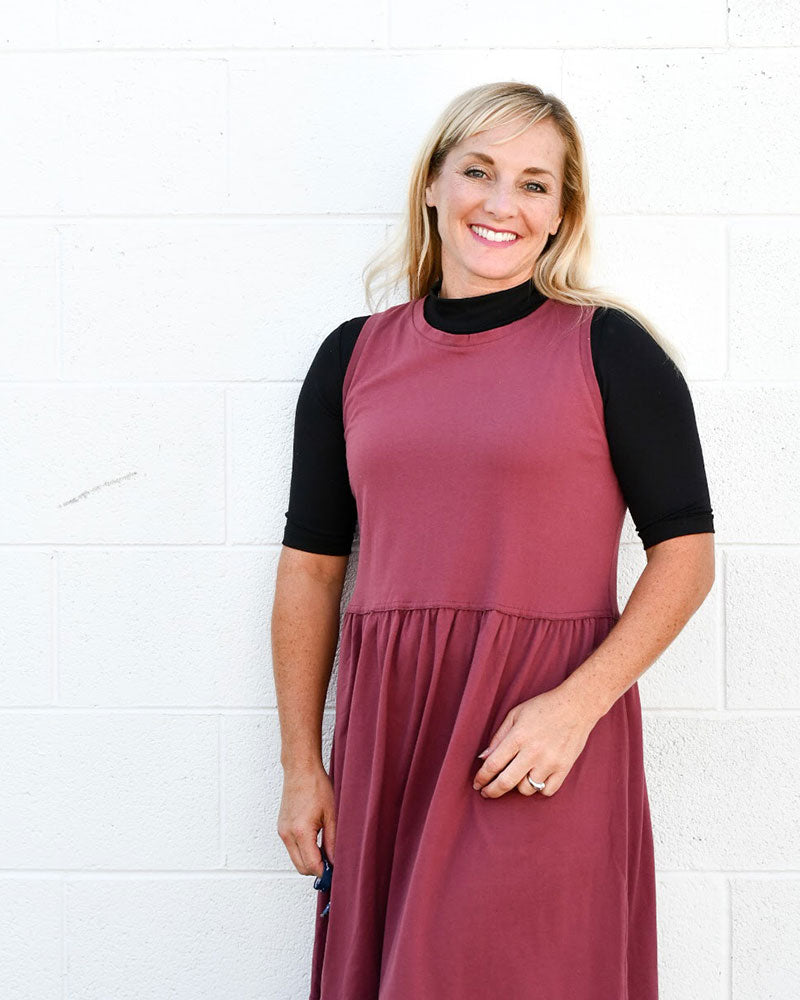 A woman wearing a burgundy dress and black turtleneck, showcasing a Mock Elbow Sleeve Halftee.