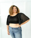 A plus size woman in a black top and jeans, wearing a Waterfall Sleeved Halftee.