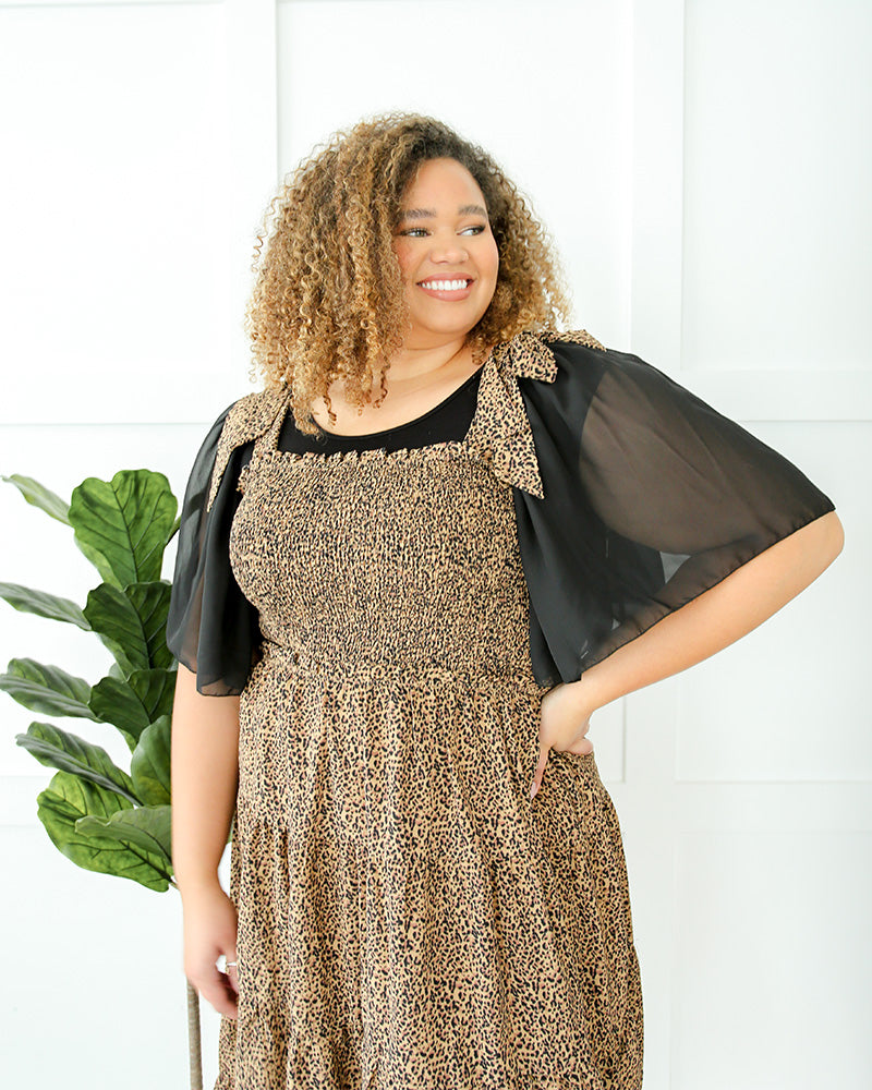A plus size woman in a black top and jeans, wearing a brown dress