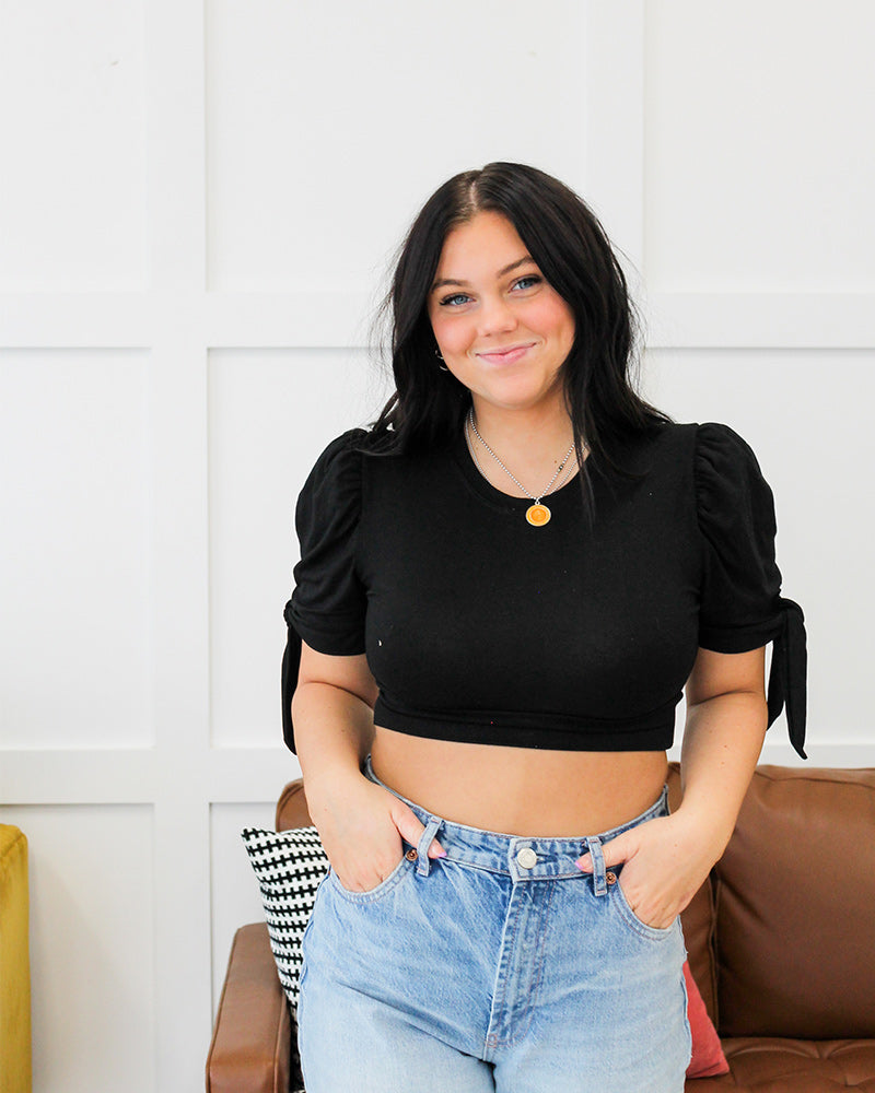 woman in a black top and jeans, wearing a Puff Sleeve Halftee with Tie Detail.