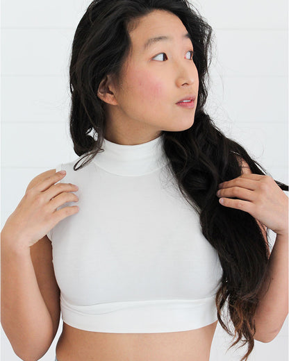 A woman wearing a white top and wide leg pants, posing in a mock neck sleeveless front outfit.