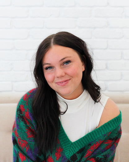 A woman in a green and red sweater sitting on a couch. 