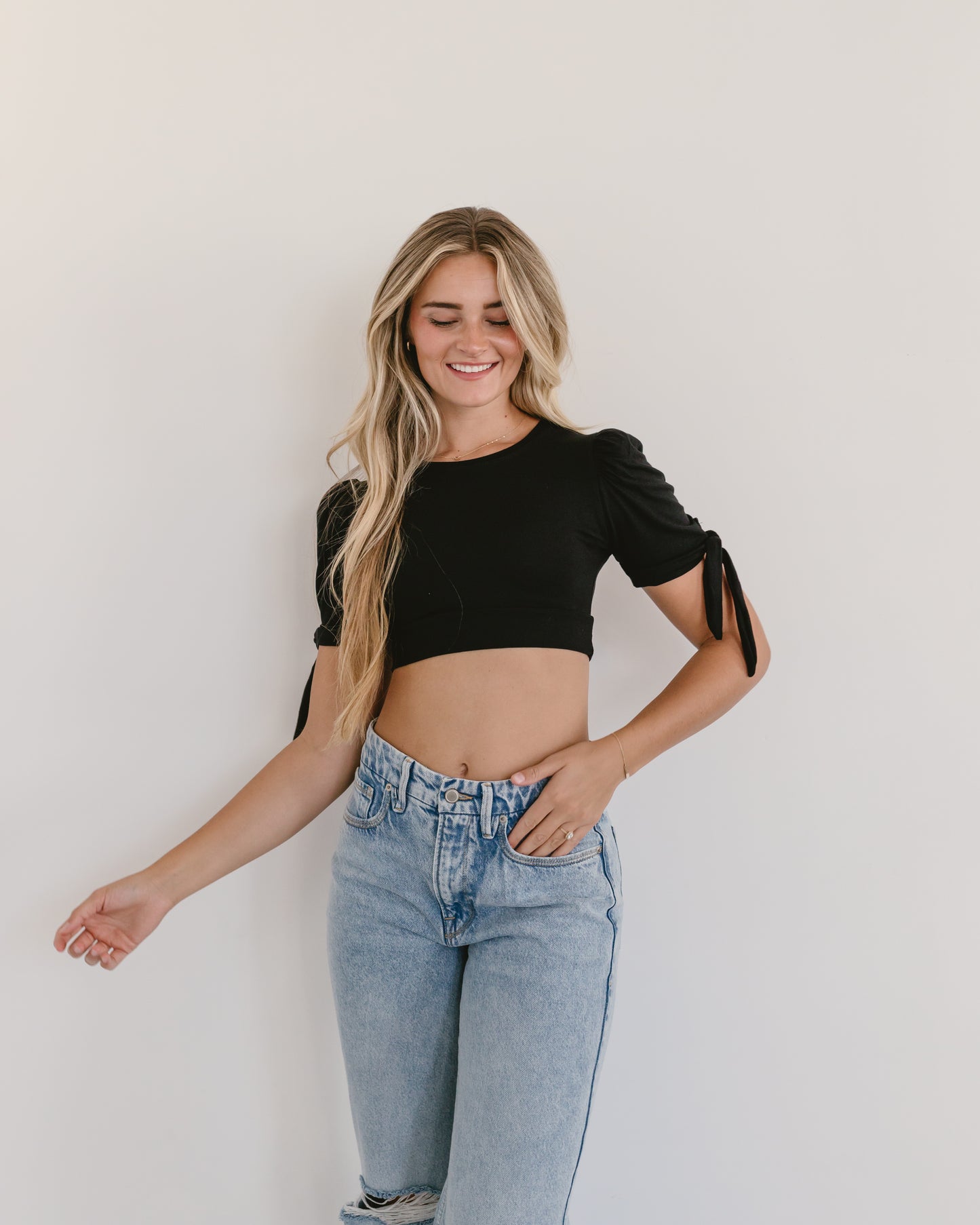 woman in a black top and jeans, wearing a Puff Sleeve Halftee with Tie Detail.